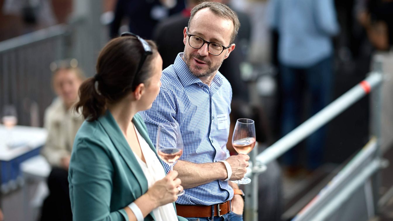 Two people are having a conversation, each holding a glass of wine.