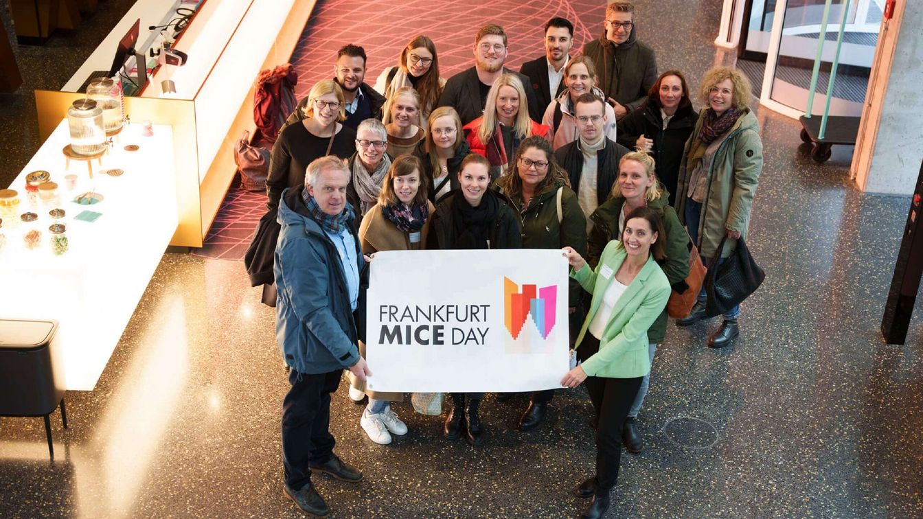 Eine Gruppe von Eventplanern, die ein Banner mit dem Logo des Frankfurt MICE DAY hält.