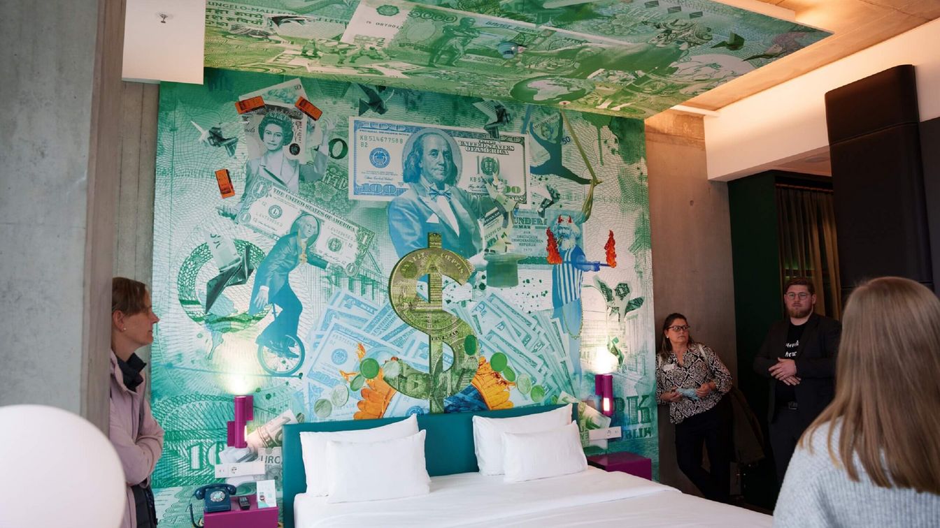 Ein Hotelzimmer, über der Rückwand des Bettes sieht man eine bunte Illustration.