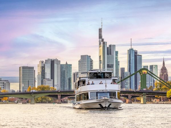 Schiff der Primus Linie in der Abenddämmerung auf dem Main mit der Frankfurter Skyline im Hintergrund.