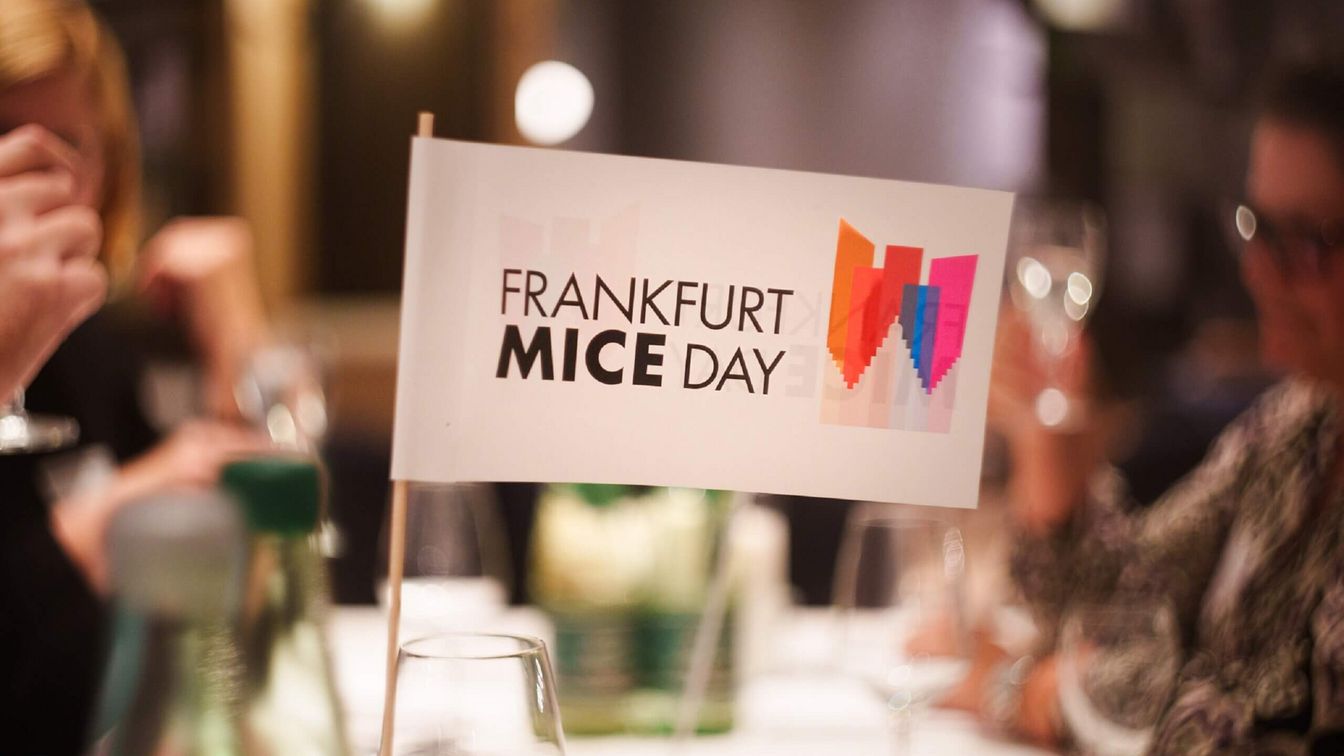 Ein Fähnchen mit dem Logo des Frankfurt MICE DAY steht auf einem eingedeckten Tisch.