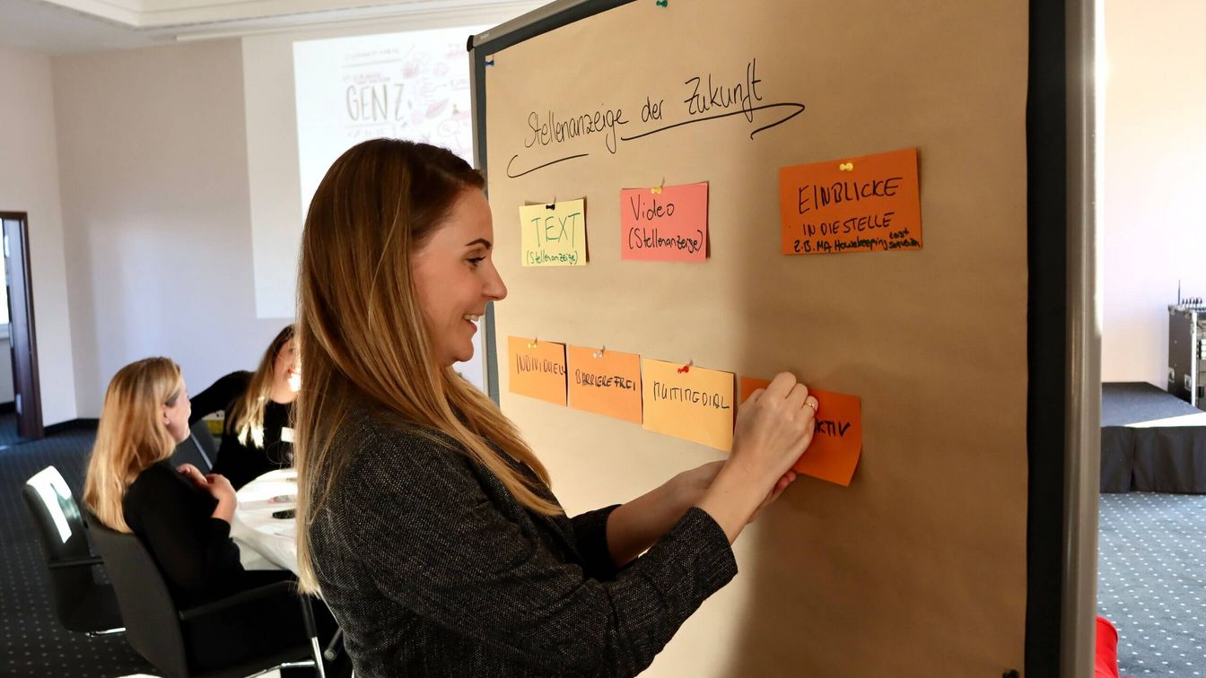 A woman stands at a pinboard and pins up a keyword on the topic of "job advertisement of the future".