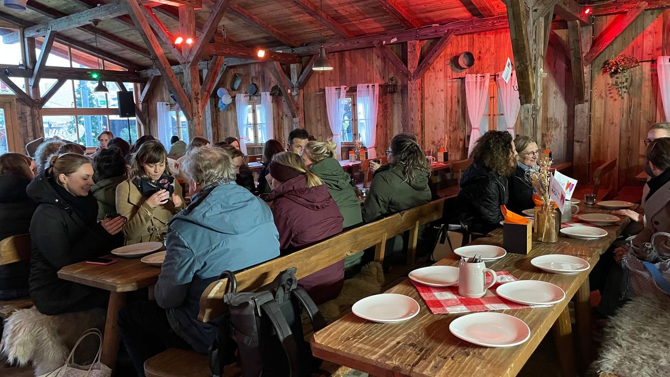 Menschen an eingedeckten Holztischen in einer Alm.